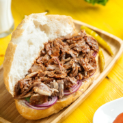 side view of beef doner in bread with pickled green pepper on a wooden platter