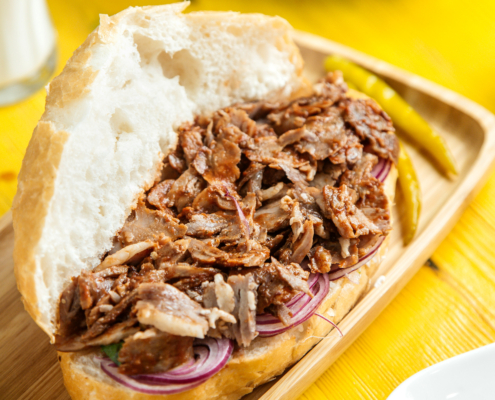 side view of beef doner in bread with pickled green pepper on a wooden platter